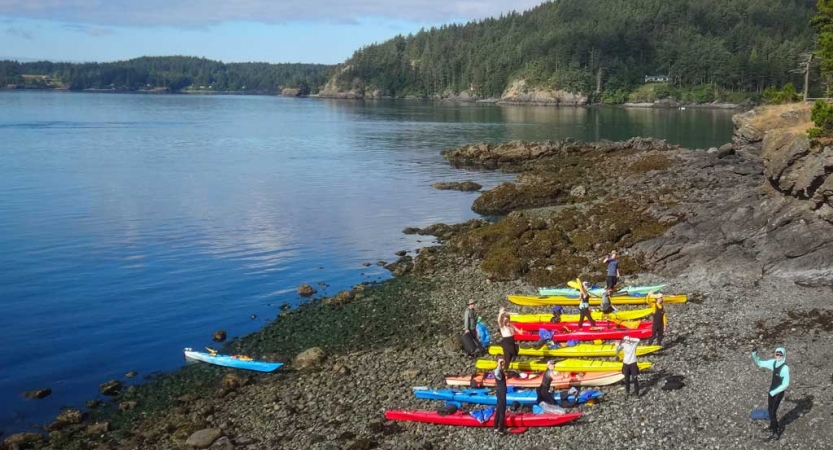 A group of colorful kayaks rest on a rocky shore beside a blue body of water